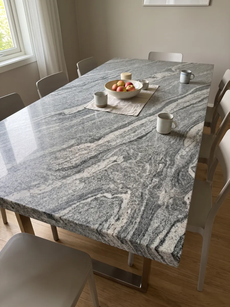Dining table with a Verde Marina granite top on a steel base: visible-grain white and grey wavy bands; the photo shows no green tones