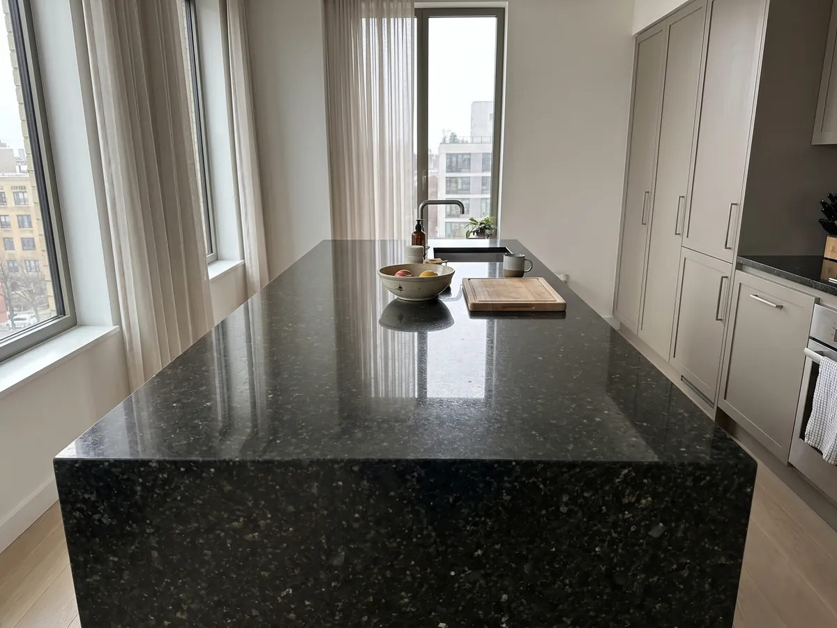 Kitchen island with a Verde Ubatuba granite countertop and a straight edge in natural light: near-black green with flashes of light green and gold