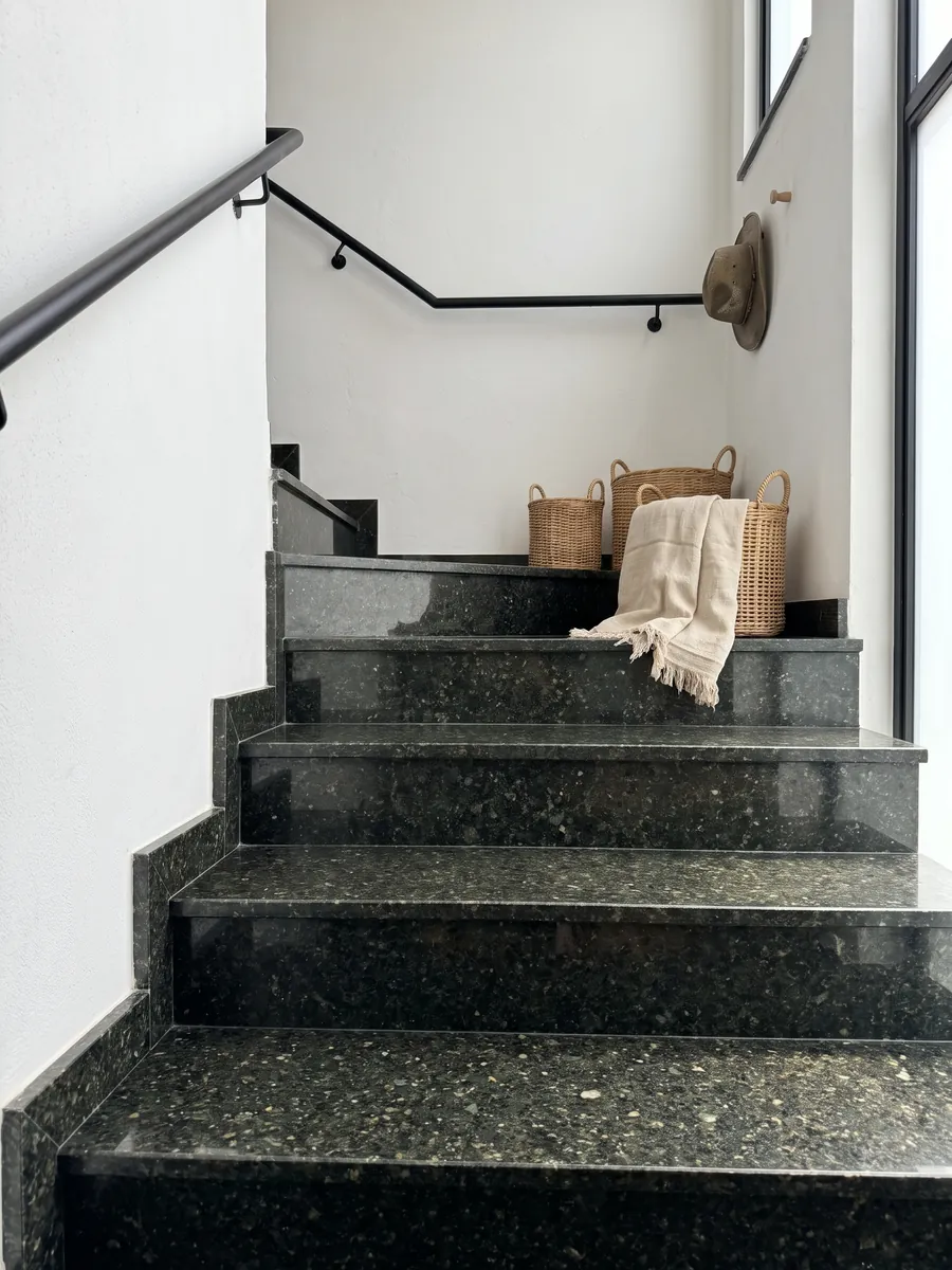Interior staircase with Verde Ubatuba granite treads and a handrail: a nearly black green with flashes of light green and gold