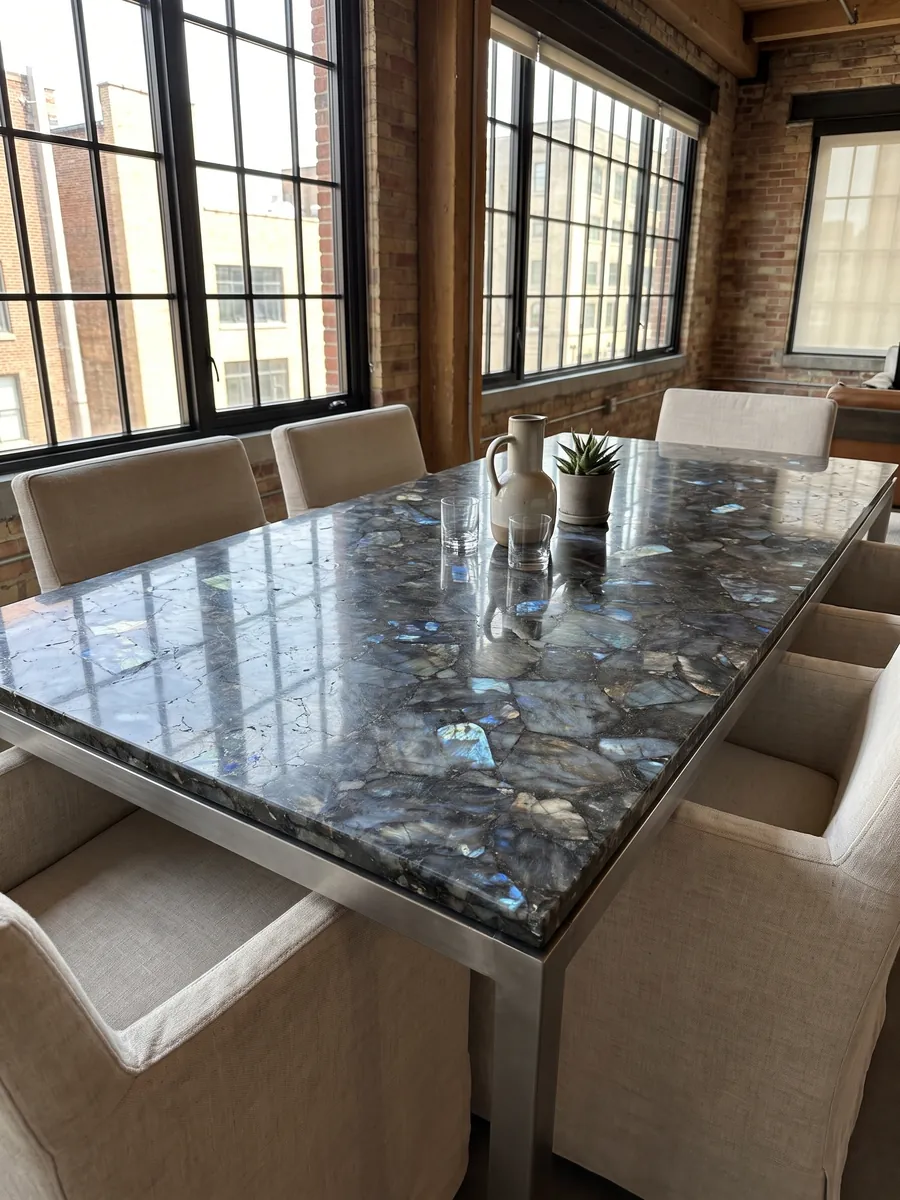 Dining table with a labradorite top on a steel base: dark gray pieces with iridescent blue flashes spread across