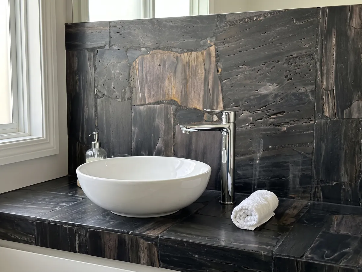 Vanity top and bathroom wall in Black Petrified Wood, Cross-Cut: dark petrified wood pieces with visible grain and a grayish brown block at the center