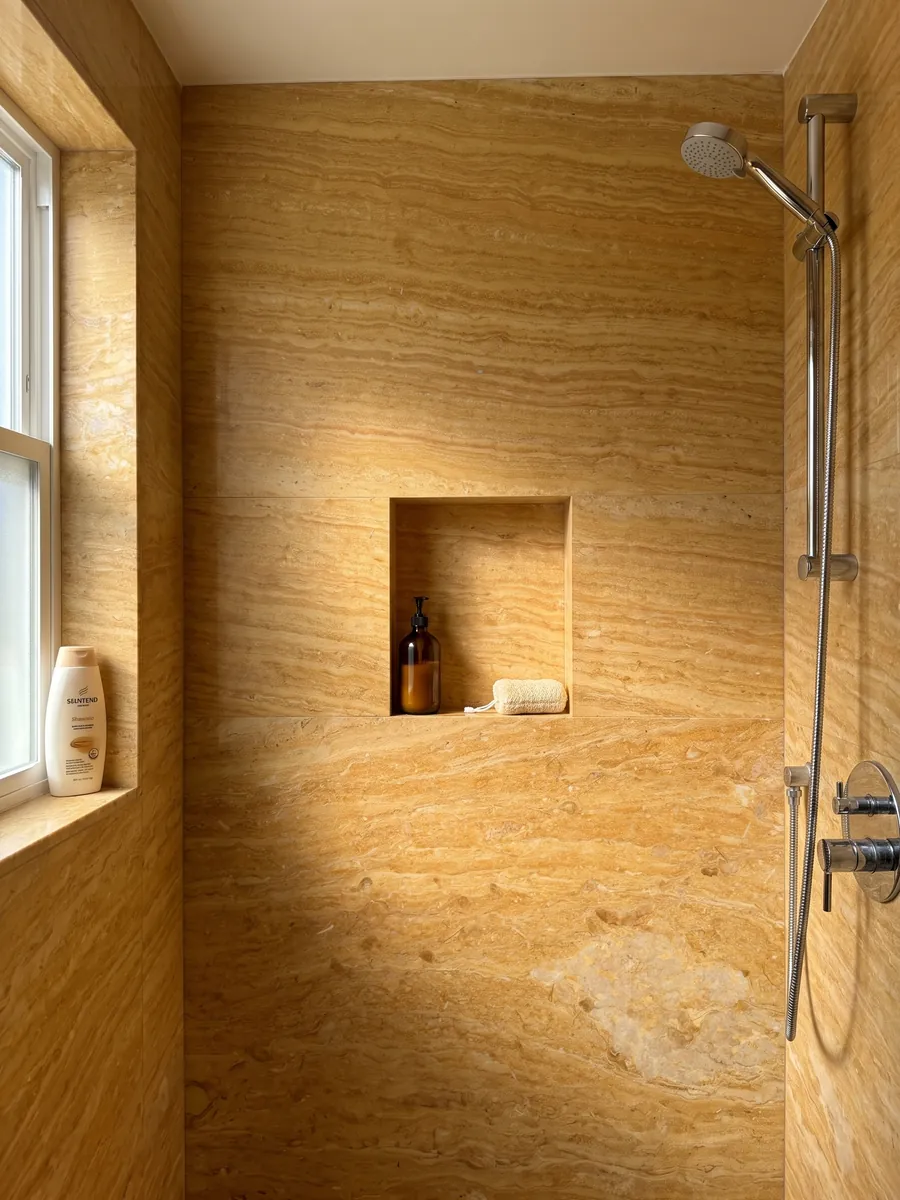 Shower clad in full Giallo Reale marble slabs with a recessed niche: intense ochre yellow with fine horizontal bands and a light beige area at the lower right