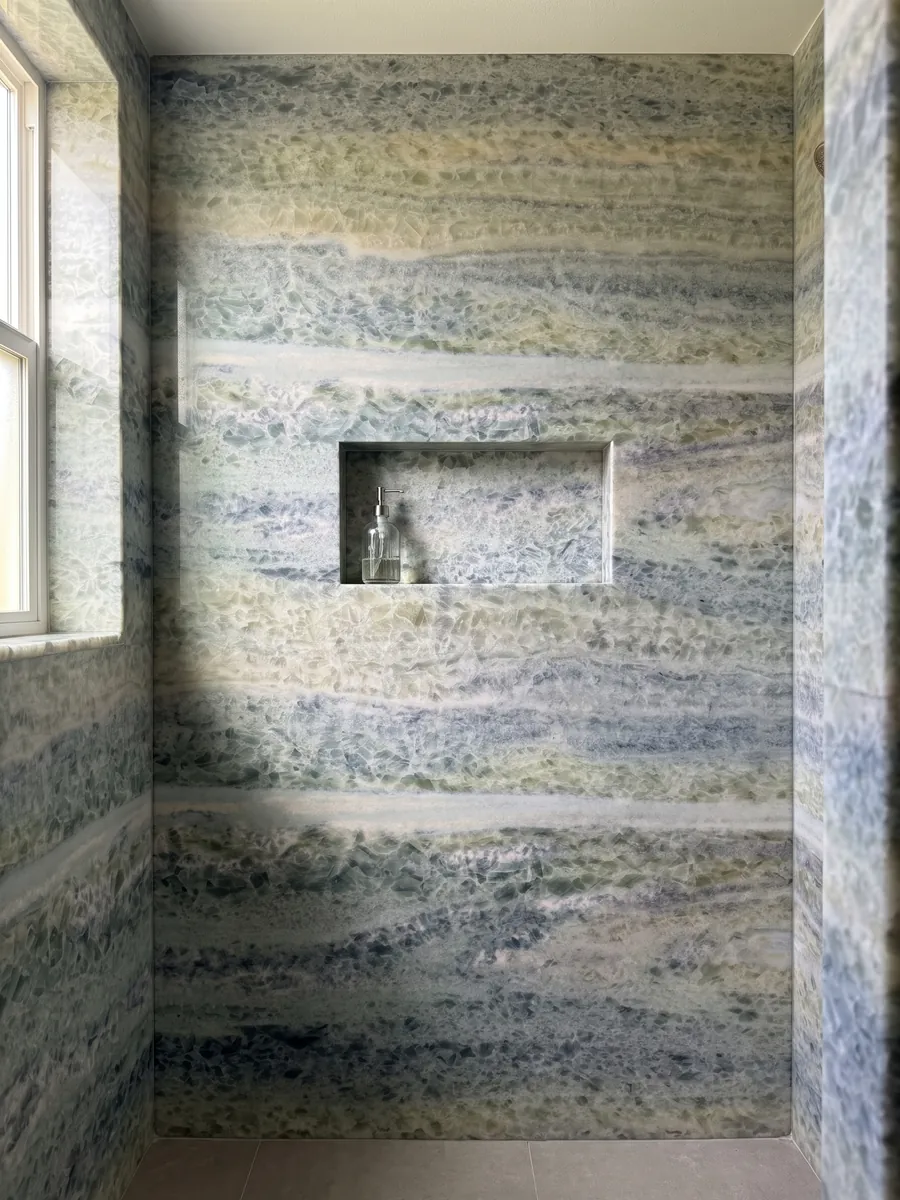 Shower clad in full slabs of blue Calcite Caraibica marble with a recessed niche: horizontal bands of blue-grey, sage green and beige crystals