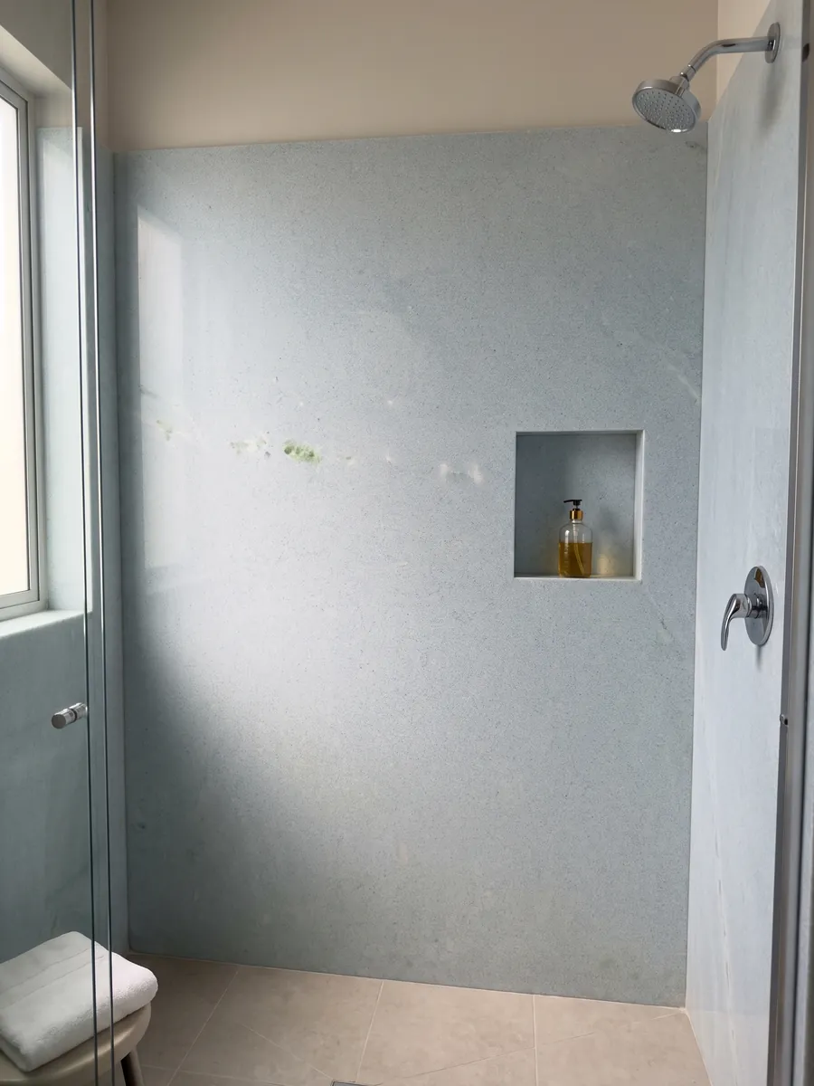 Shower clad in full slabs of Azul Cielo marble with a recessed niche: nearly uniform pale sky blue, fine-grained, with a green inclusion on the left