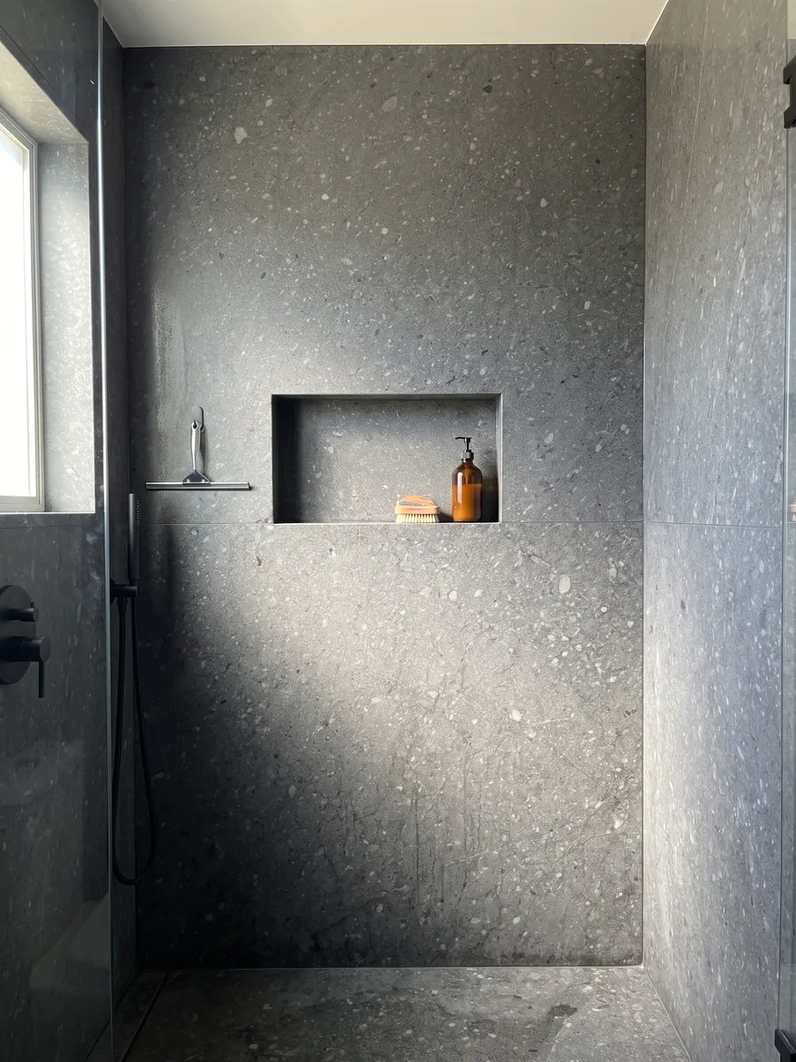 Shower clad in full slabs of Blu Masaccio marble with a recessed niche: uniform dark gray with small speckles and lighter gray fragments