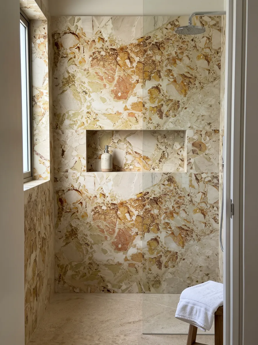Shower clad in whole beige Alma Fuoco marble slabs with a recessed niche: ocher and rust stains with crisp edges grouping in the upper central area