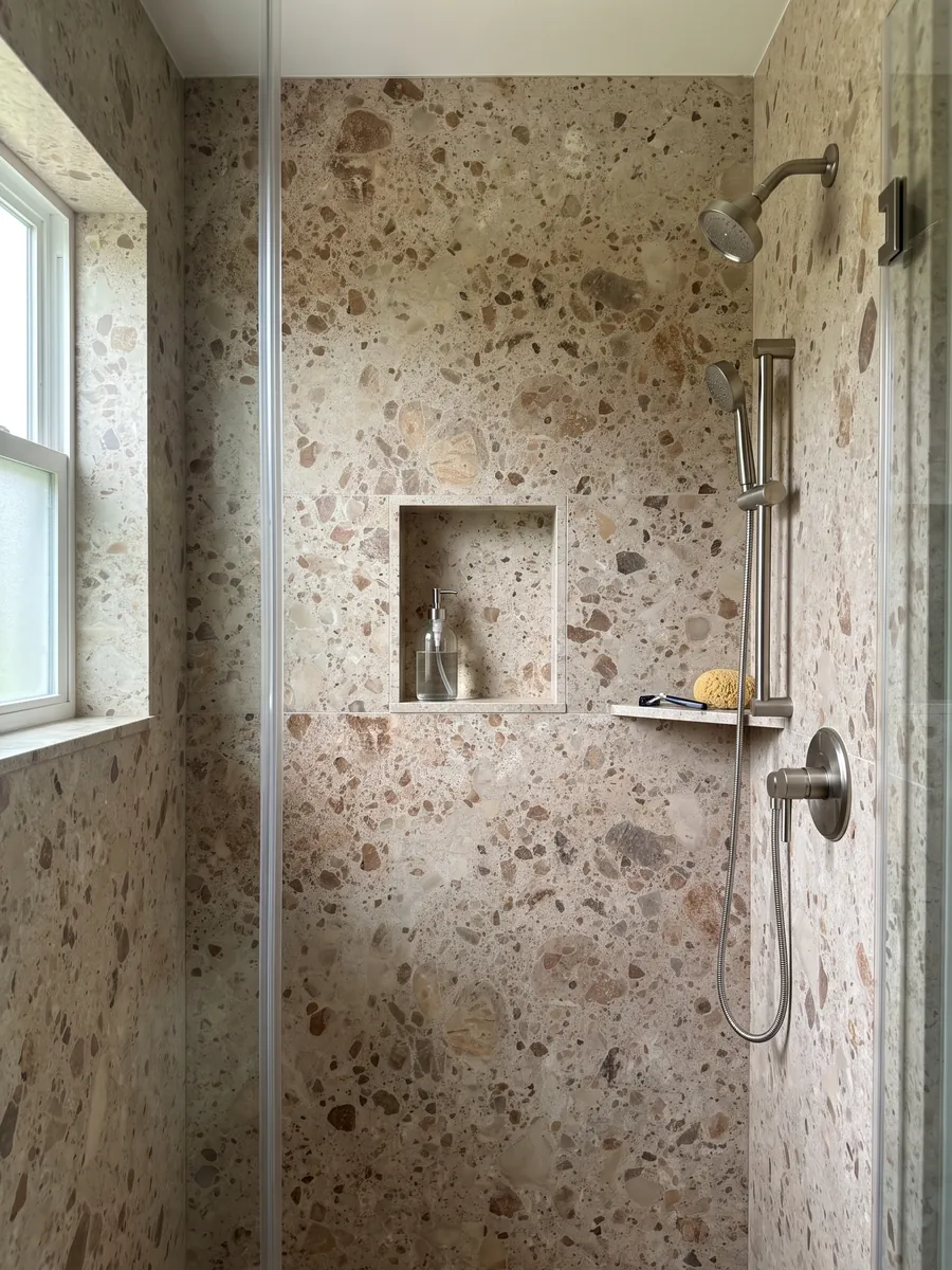 Shower clad in full slabs of beige Ambrosia marble with a recessed niche: beige matrix with rounded brown and rust fragments in several sizes