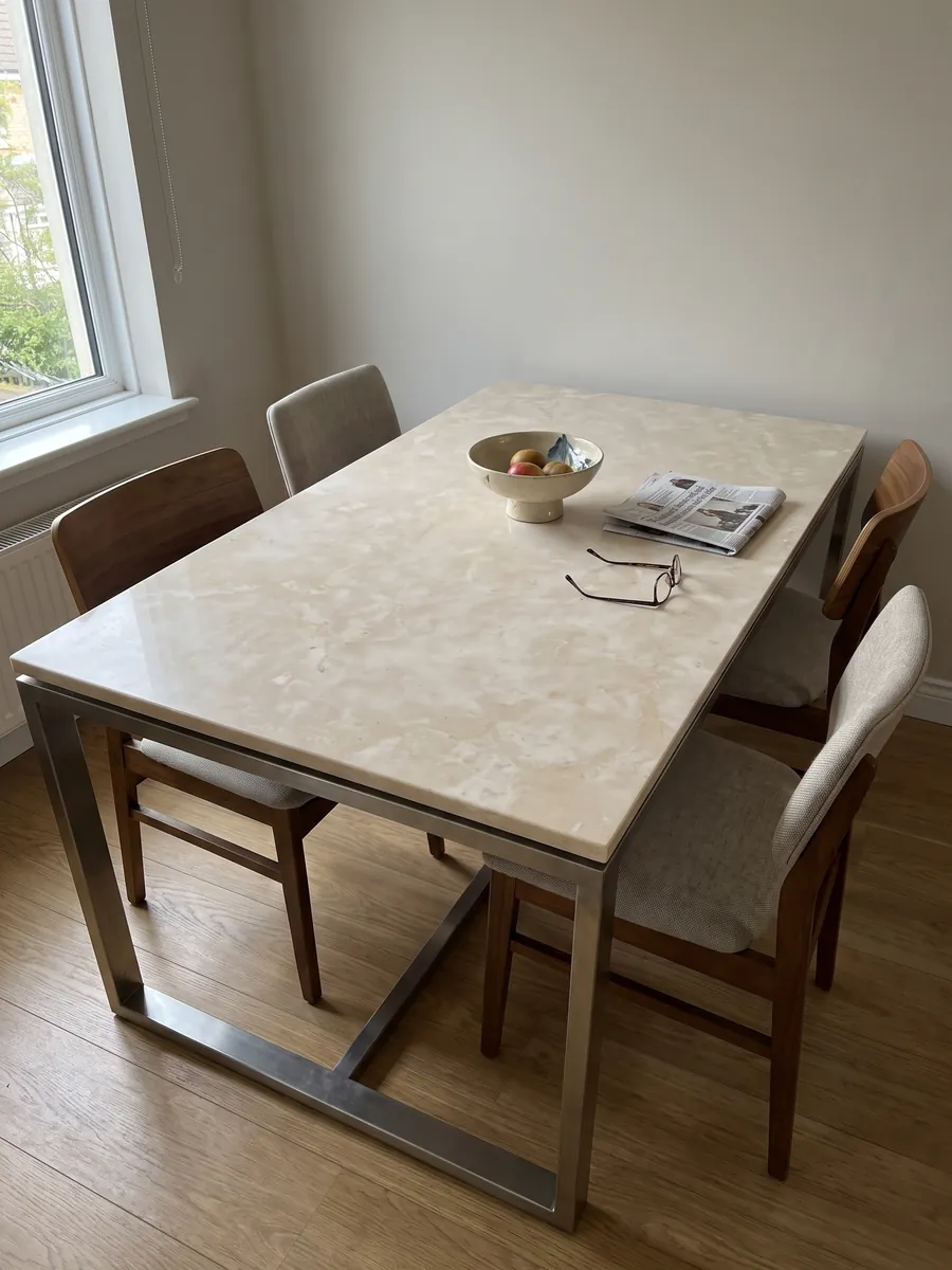 Dining table with a beige Botticino marble top on a steel base: a warm, almost uniform cream with soft clouds