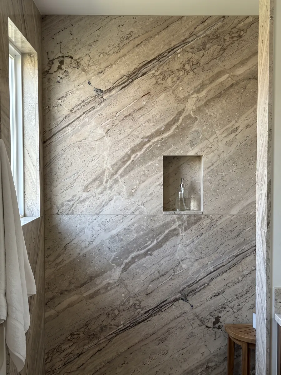 Shower clad in full slabs of Breccia Aurora beige marble with a recessed niche: grayish beige with parallel brown veins running diagonally and a more streaked area at the bottom