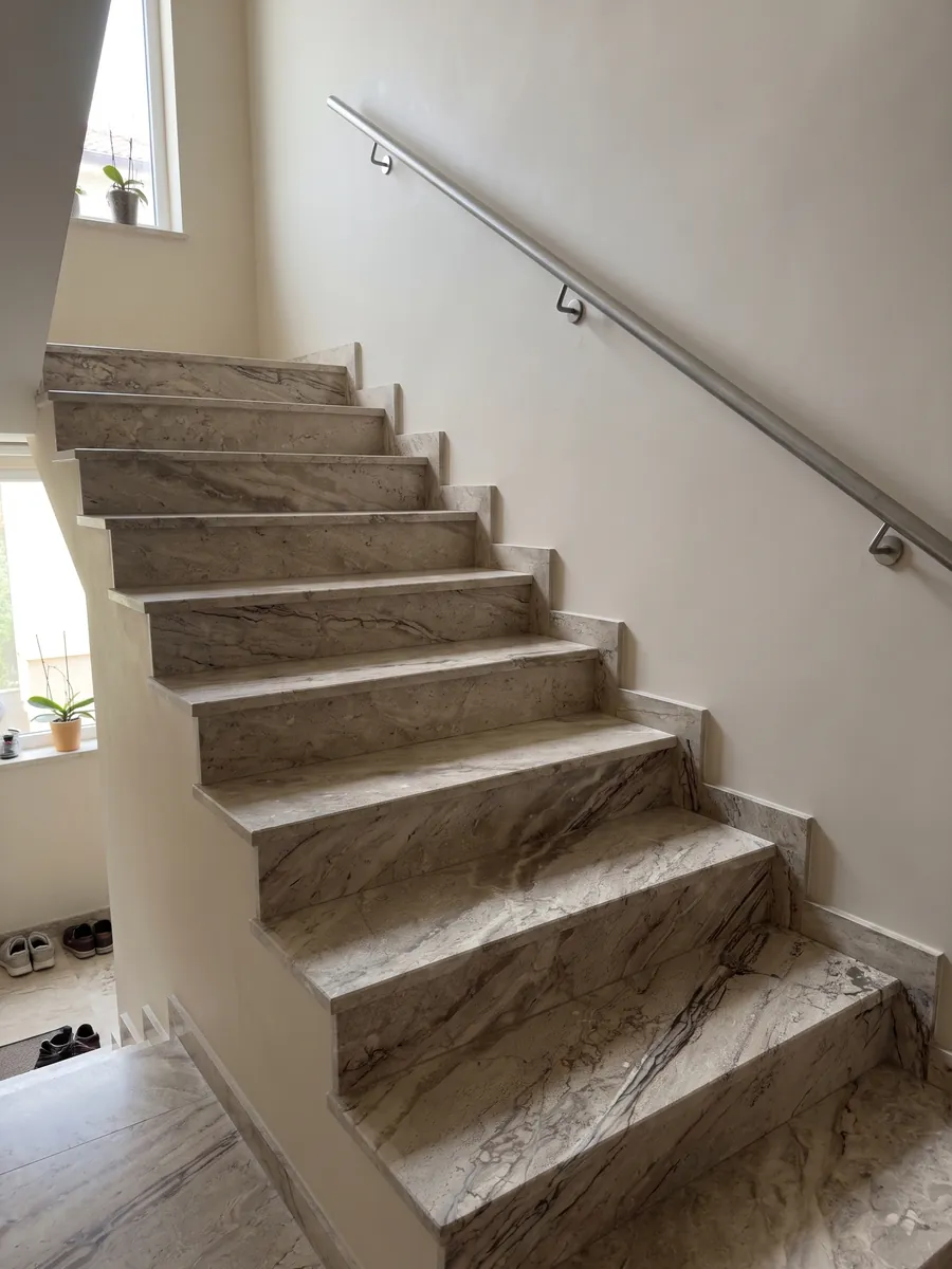 Indoor staircase with Breccia Aurora beige marble steps and a handrail: grayish beige with parallel brown veins running diagonally and a more streaked area at the bottom
