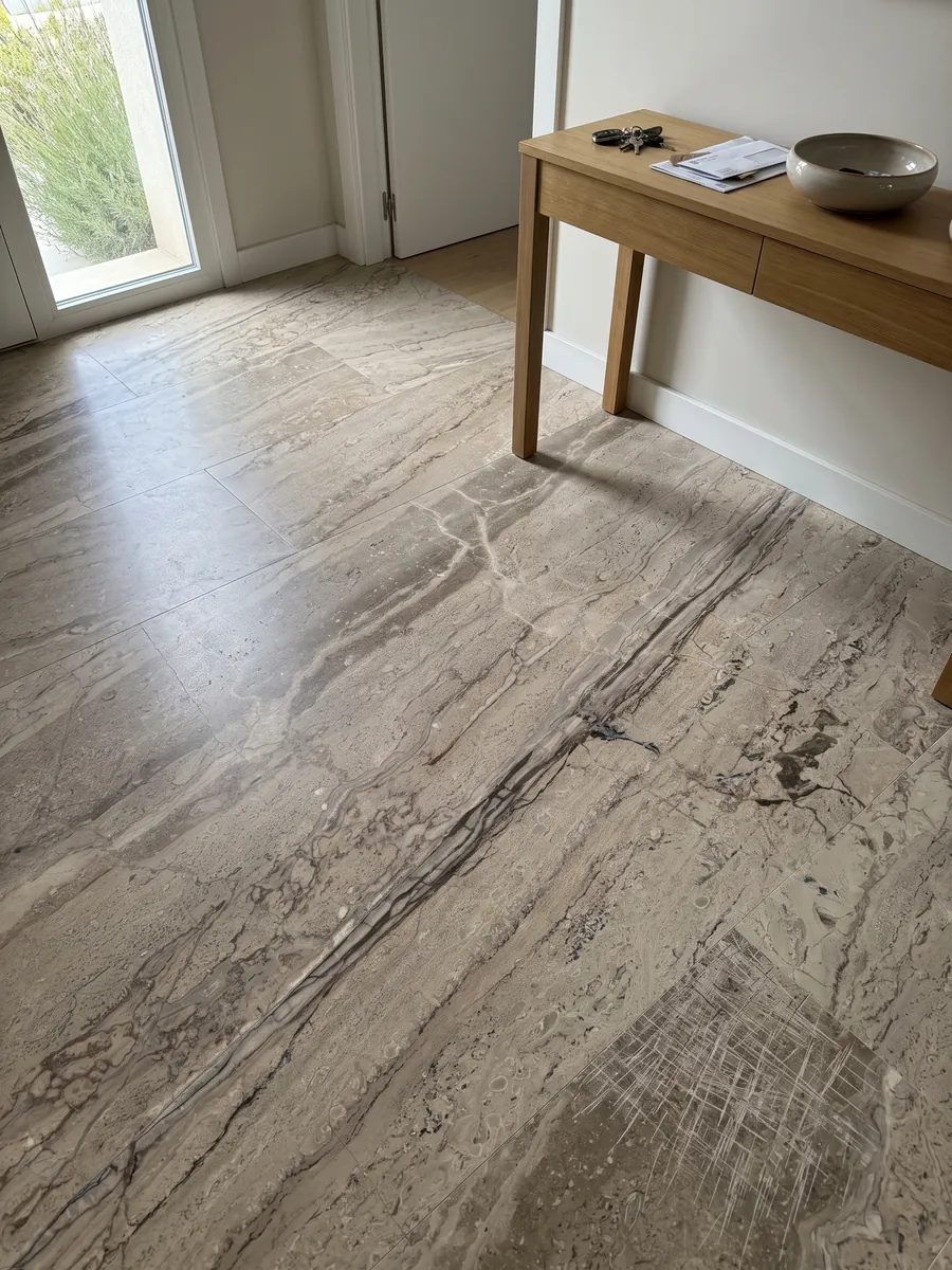 Entryway floor in large slabs of Breccia Aurora beige marble with natural light: grayish beige with parallel brown veins running diagonally and a more streaked area at the bottom