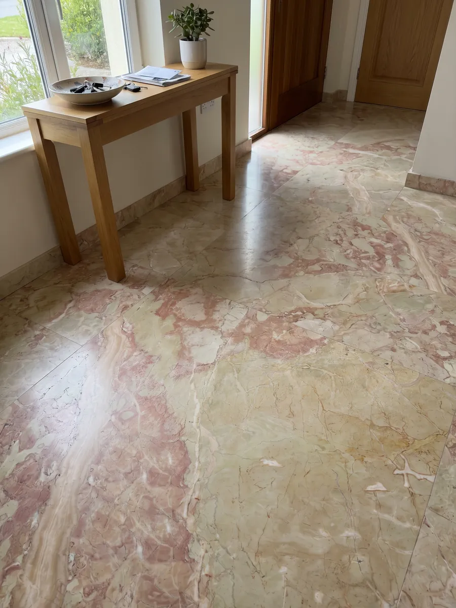 Entryway floor in large slabs of beige Breccia D'Aragona marble in natural light: large greenish beige fragments with coral pink patches along the left edge
