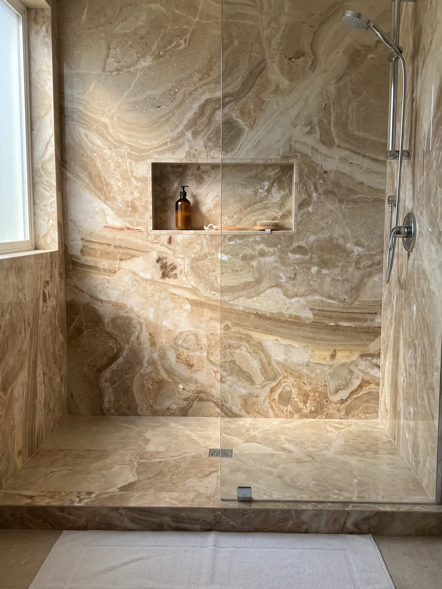 Shower clad in full Breccia Oniciata beige marble slabs with a recessed niche: golden beige fragments with concentric waves and a striped brown band at the bottom