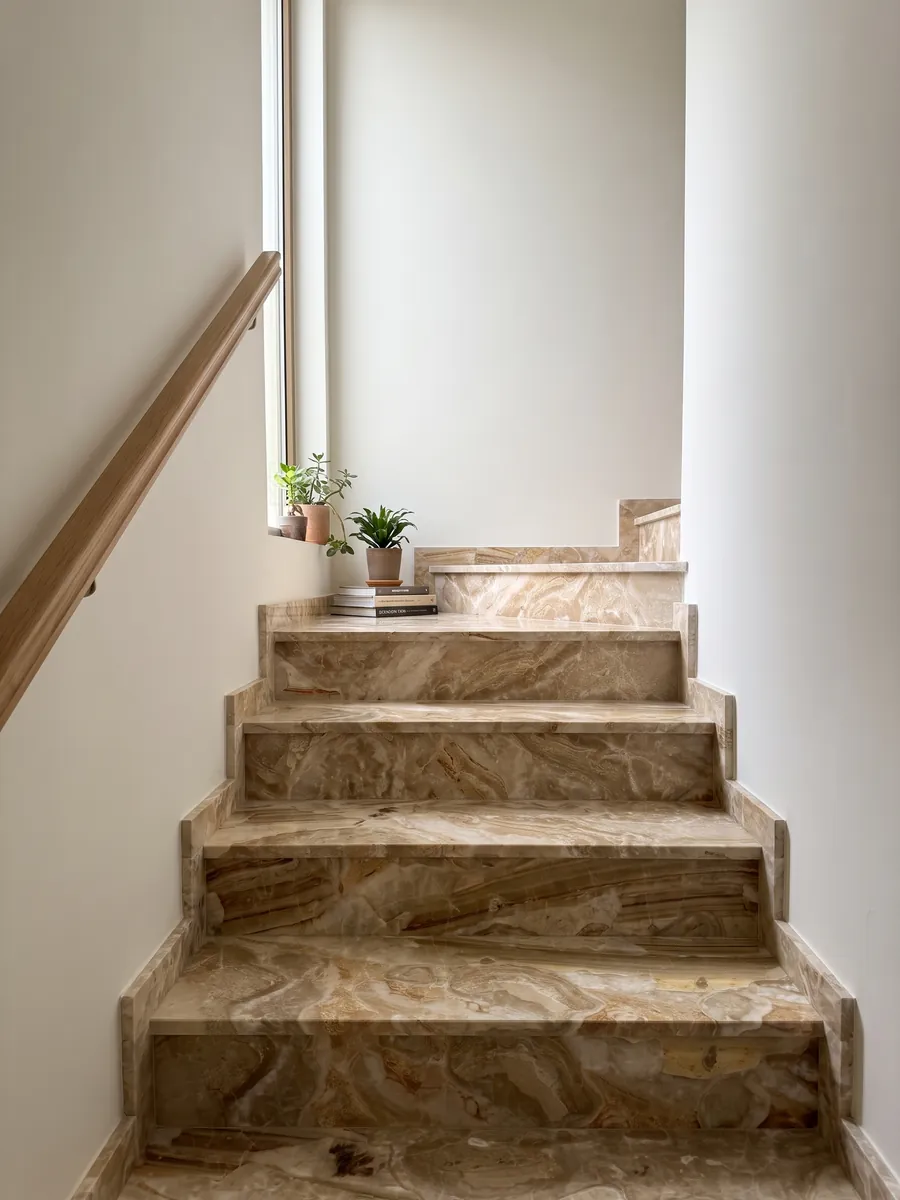 Indoor staircase with Breccia Oniciata beige marble steps and a handrail: golden beige fragments with concentric waves and a striped brown band at the bottom