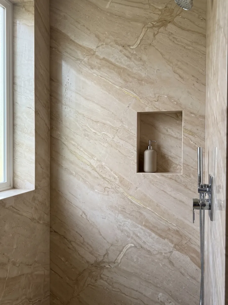 Shower clad in full slabs of beige Breccia Sarda marble with a recessed niche: warm beige with diagonal cream and light brown veins