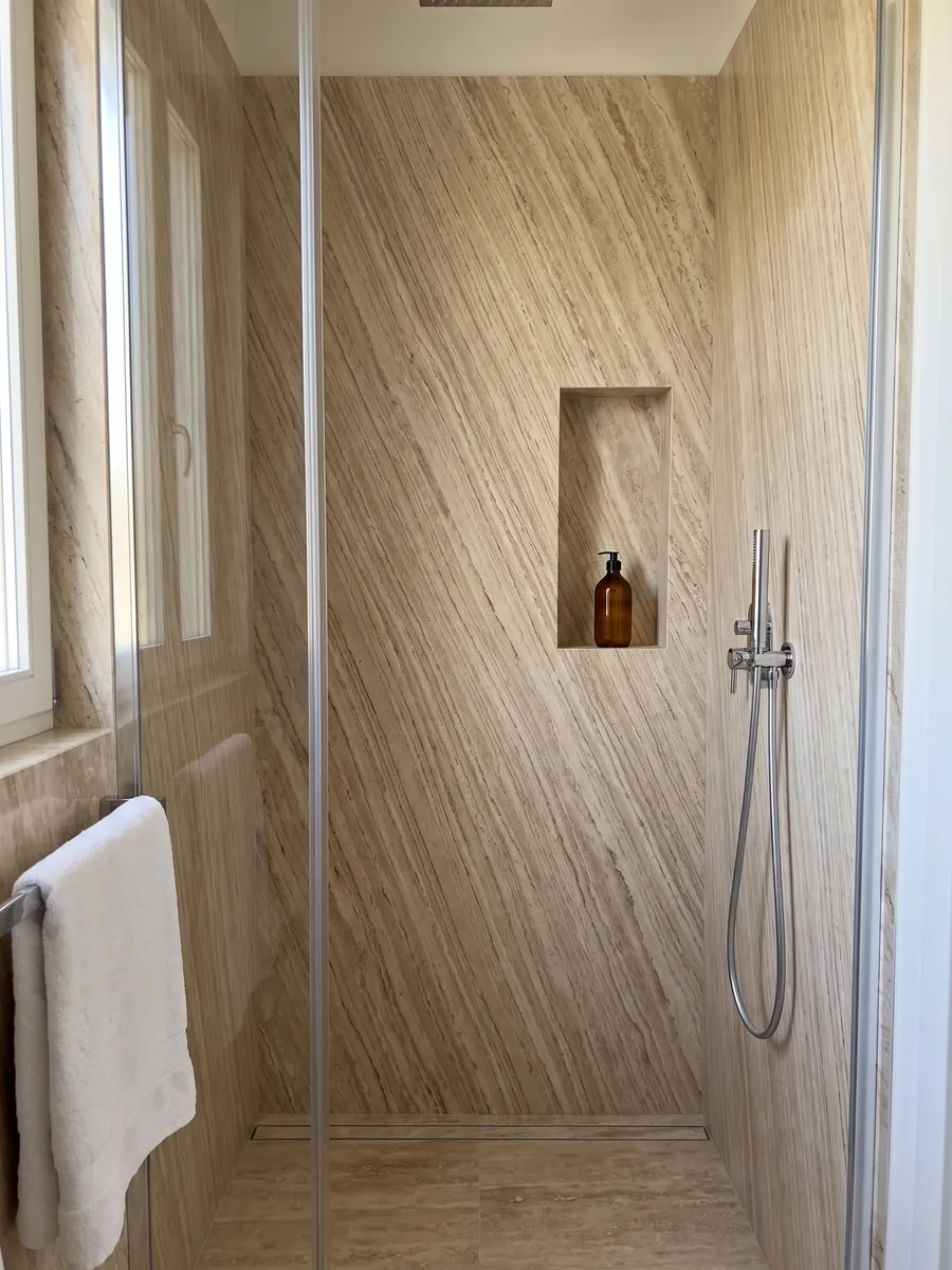Shower clad in full slabs of beige Daino Reale marble with a recessed niche: beige with fine parallel veins running diagonally like wood grain