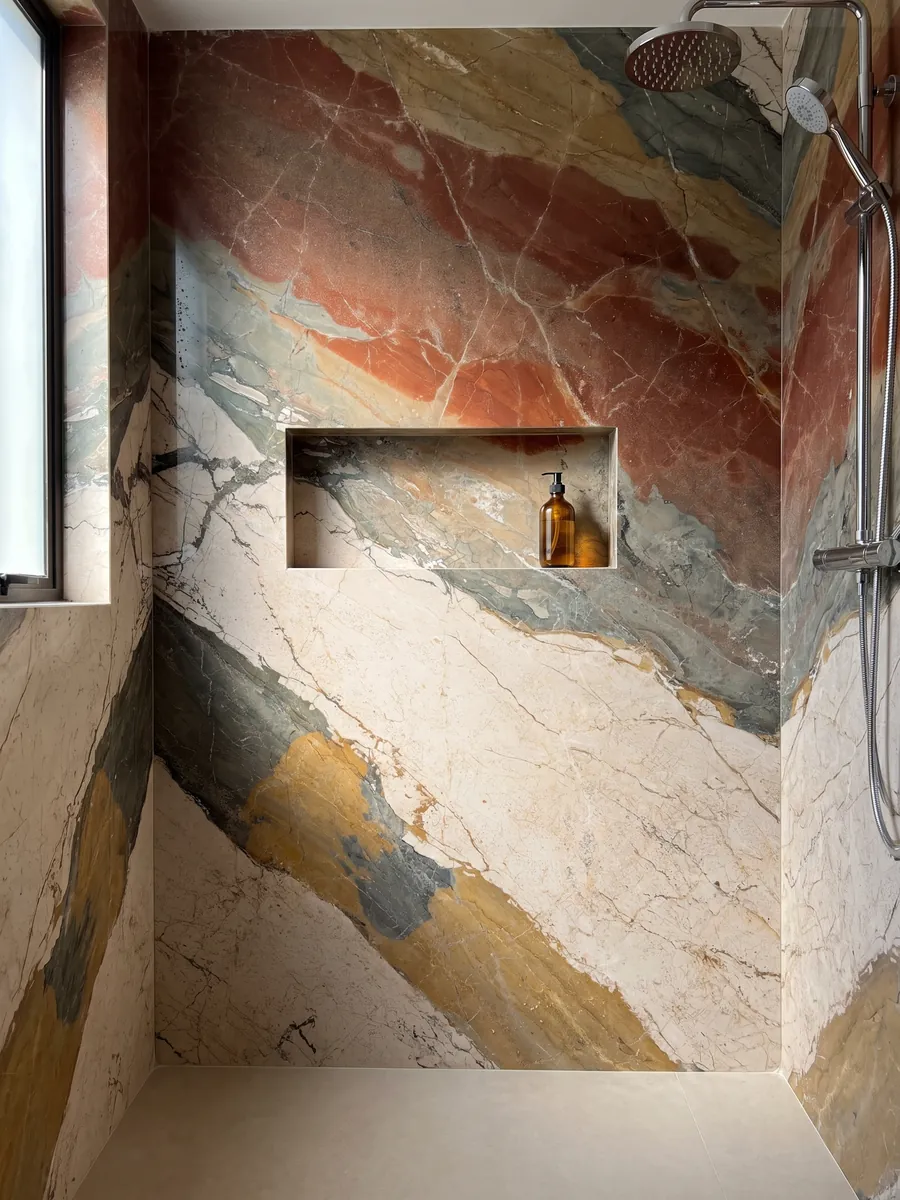 Shower clad in full slabs of beige Etna marble with a recessed niche: diagonal bands of four very different colors: cream, greenish gray, ochre and rust red