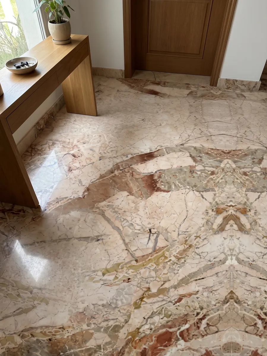 Foyer floor in large beige Golden Vein marble slabs in natural light: pinkish beige fragments separated by terracotta patches; the pattern looks like a mirror image