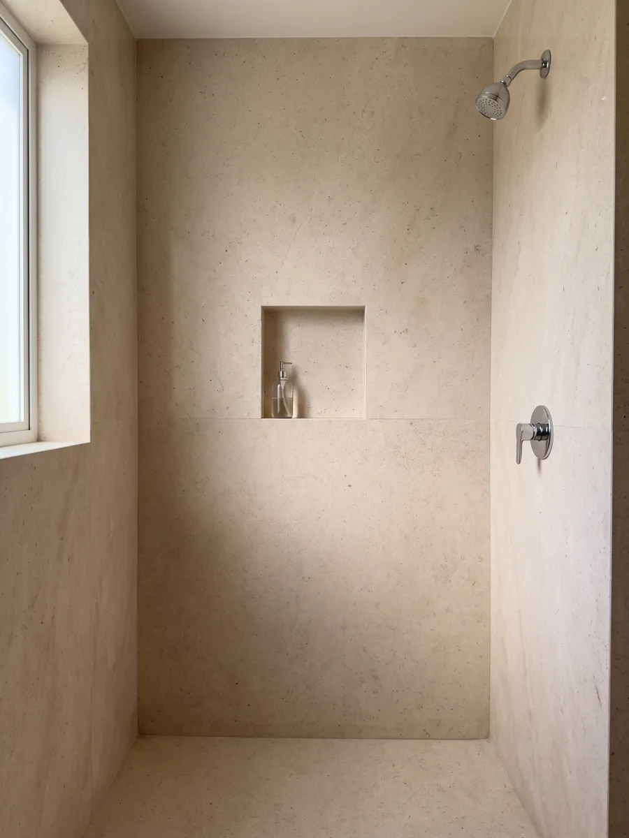 Shower clad in full beige Masai marble slabs with a recessed niche: light, even pinkish cream, fine-grained with no veins