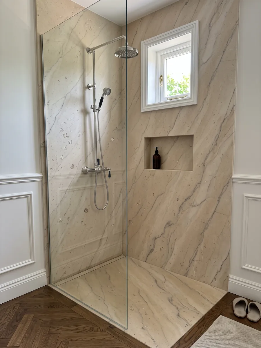 Shower clad in full Beige Maya marble slabs with a recessed niche: warm beige with soft gray veins and small fossils