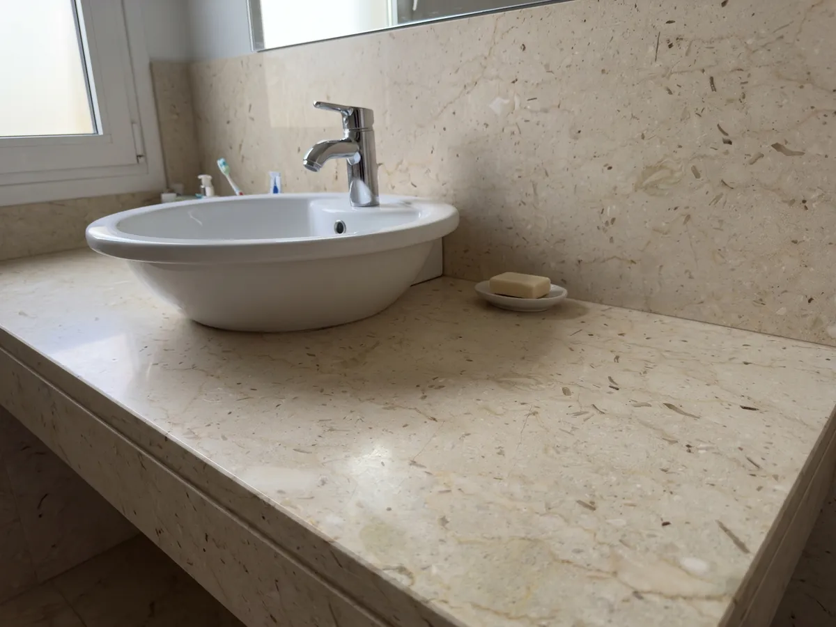 Bathroom vanity top and wall in beige Pietra Ducale marble with a white sink and chrome faucets: yellowish cream with small fossil fragments and brown dots