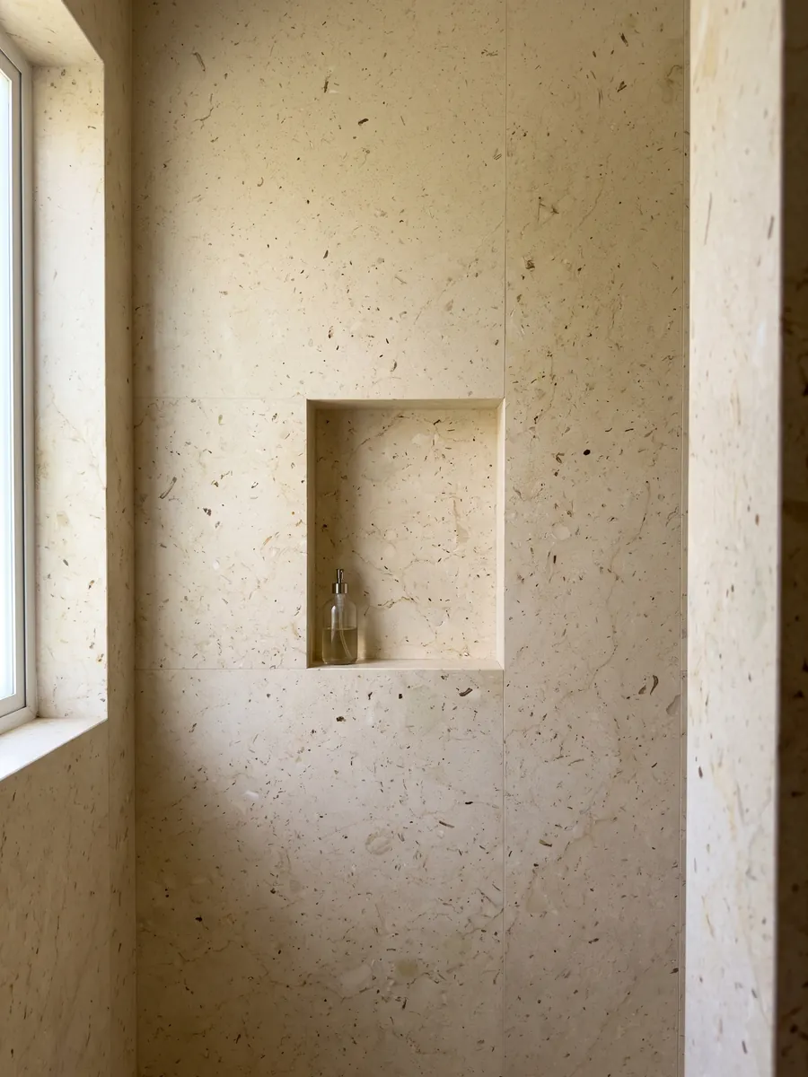Shower clad in full beige Pietra Ducale marble slabs with a recessed niche: yellowish cream with small fossil fragments and brown dots