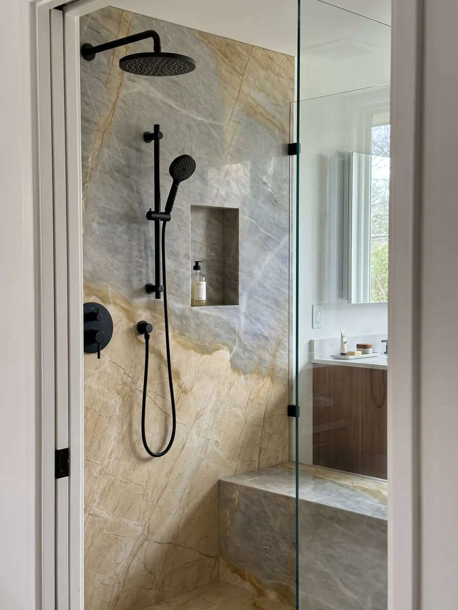 Shower clad in full slabs of beige Skysand marble with a recessed niche: one golden yellow zone and one bluish gray zone separated by an ochre line