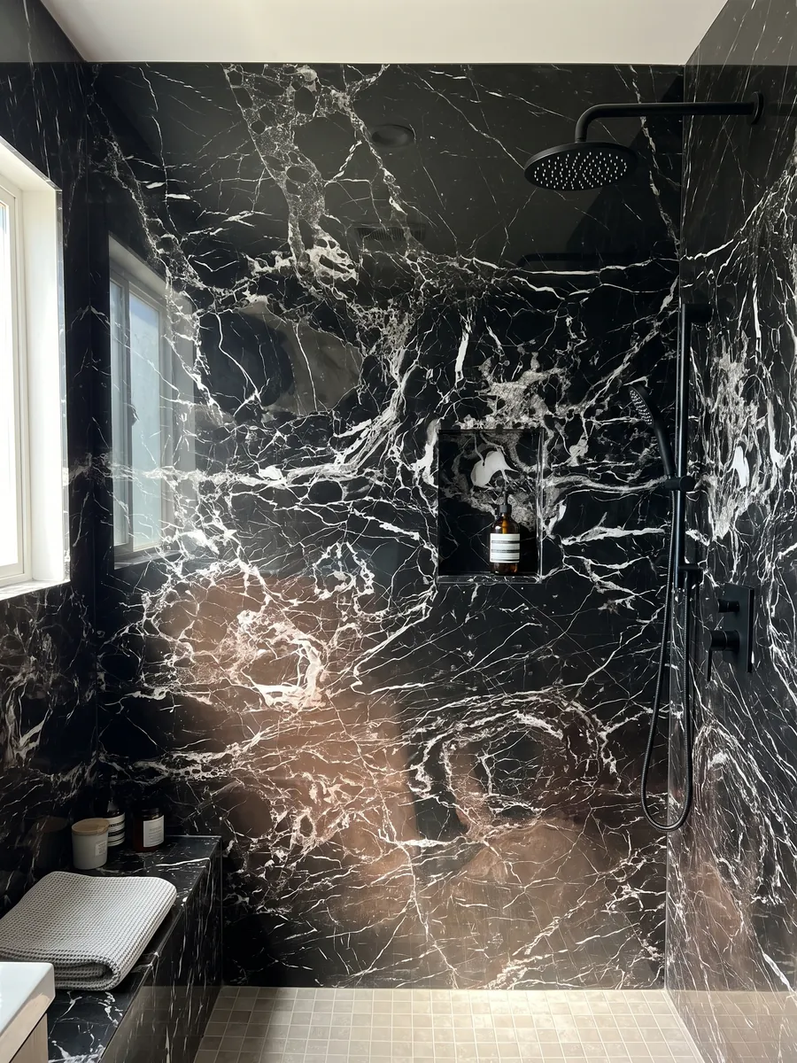 Shower clad in full slabs of Black Rose marble with a recessed niche: black with a dense web of white veins and a lower area with a brown tint