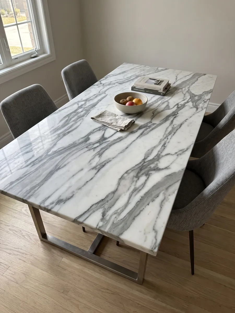 Dining table with a white Arabescato Apuano marble top on a steel base: thick, branching dark gray veins crossing the white diagonally