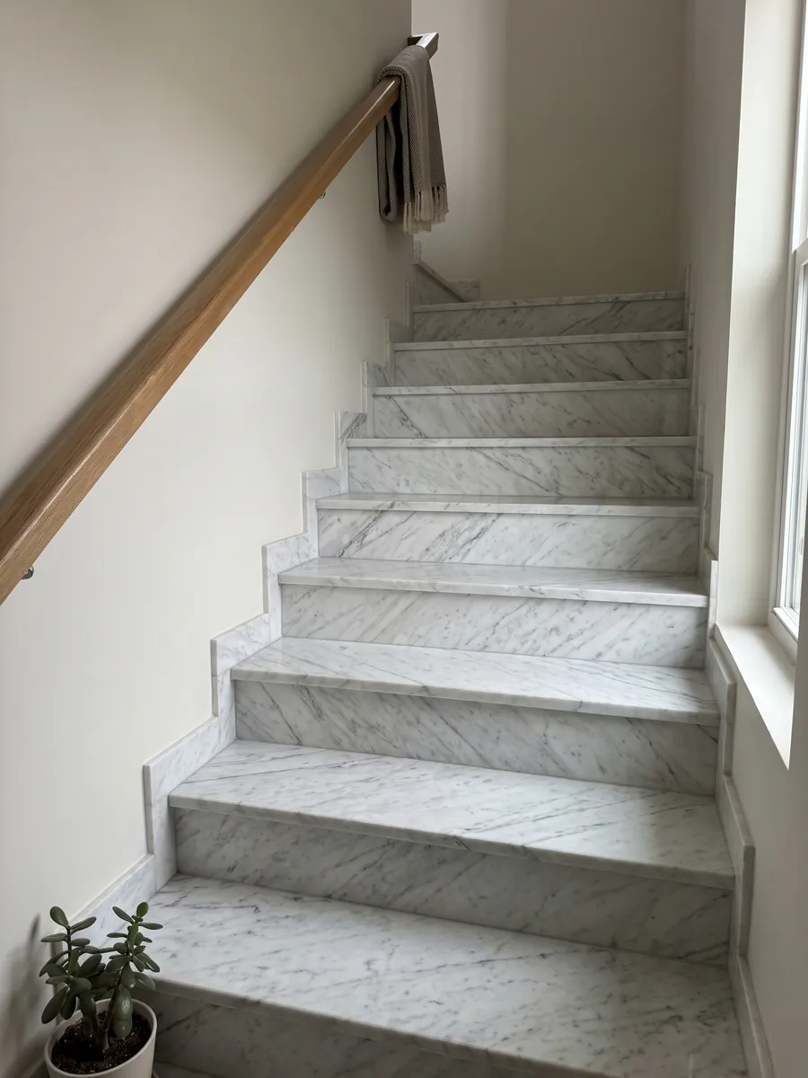 Interior staircase with white Calacatta Classic marble steps and handrail: white with fine light gray veins running diagonally across the slab
