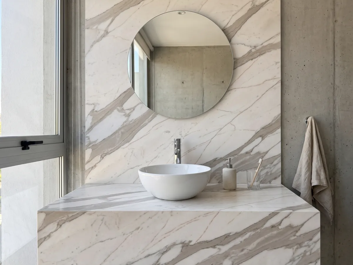 Bathroom vanity top and wall in white Calacatta Cremo marble with a white sink and chrome fixtures: ivory white with wide beige gray veins and fine copper lines