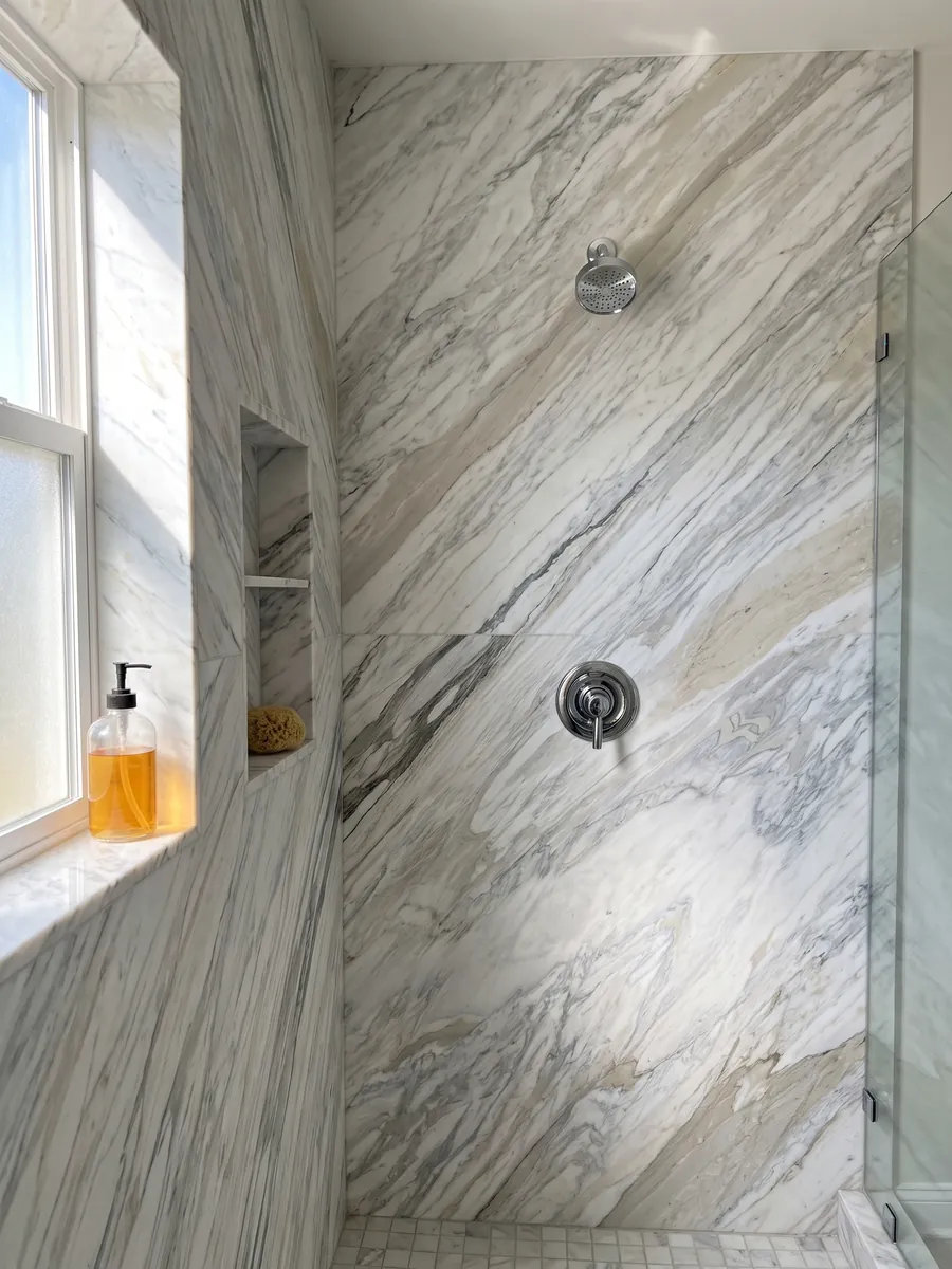 Shower clad in full slabs of white Calacatta Manhattan marble with a recessed niche: white with fine, soft gray veins that flow on the diagonal