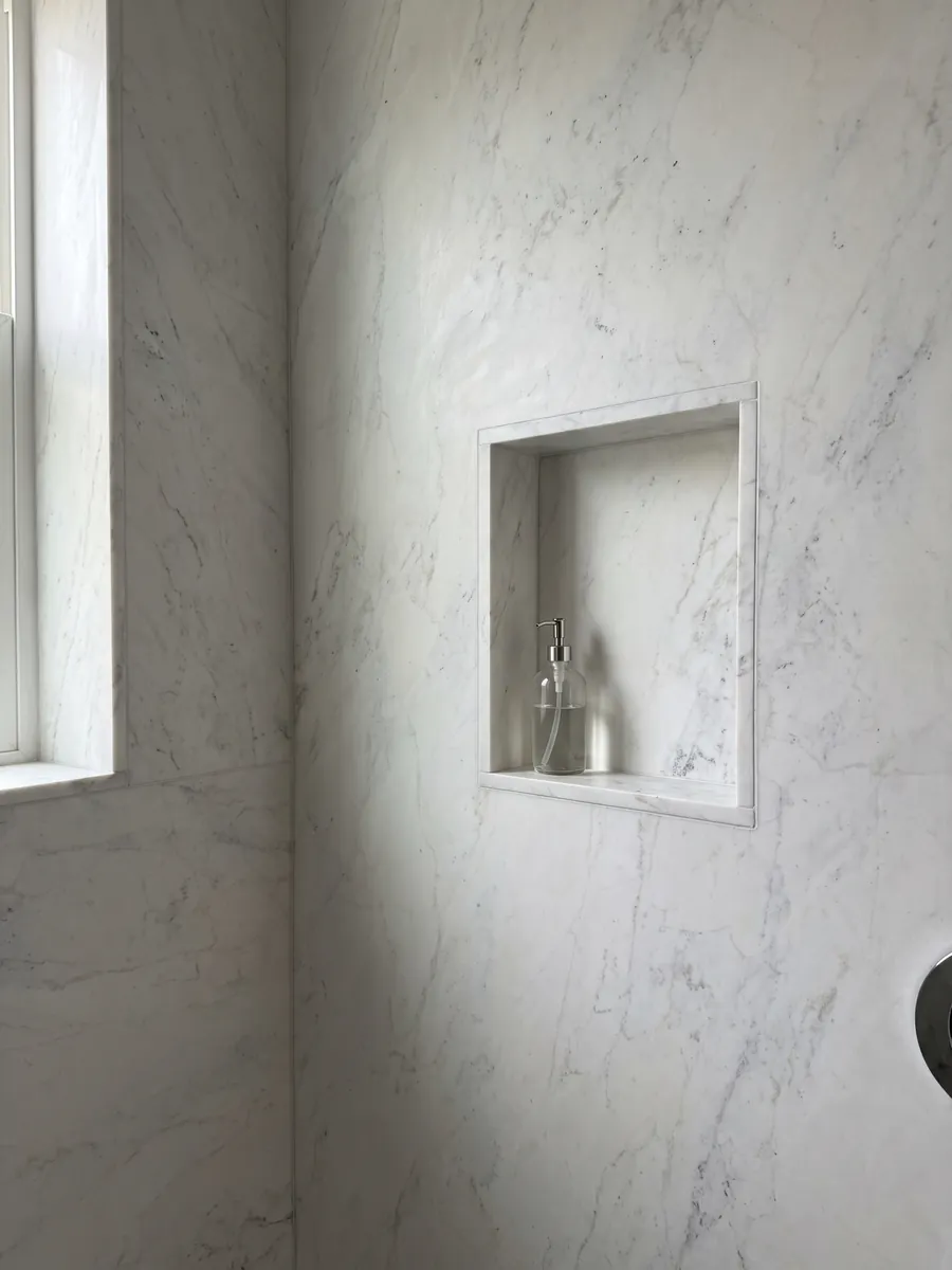 Shower clad in full slabs of white Calacatta Michelangelo marble with a recessed niche: almost smooth grayish white with a few very soft gray marks
