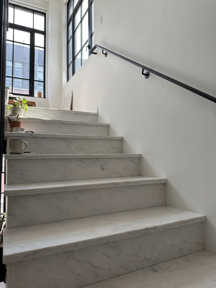 Interior staircase with white Calacatta Michelangelo marble steps and a handrail: almost smooth grayish white with a few very soft gray marks