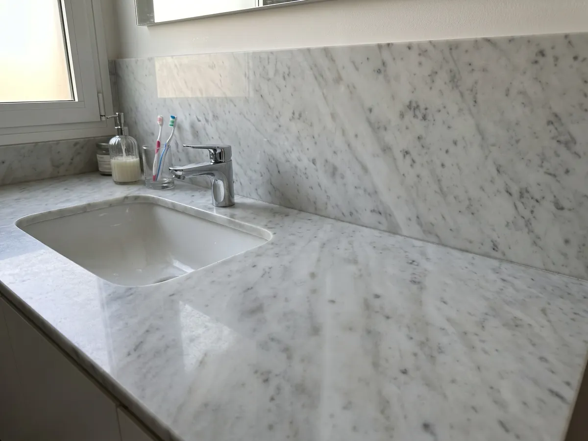 Vanity top and bathroom wall in white Carrara CD marble with a white sink and chrome fixtures: grayish white with diffuse gray patches on the diagonal