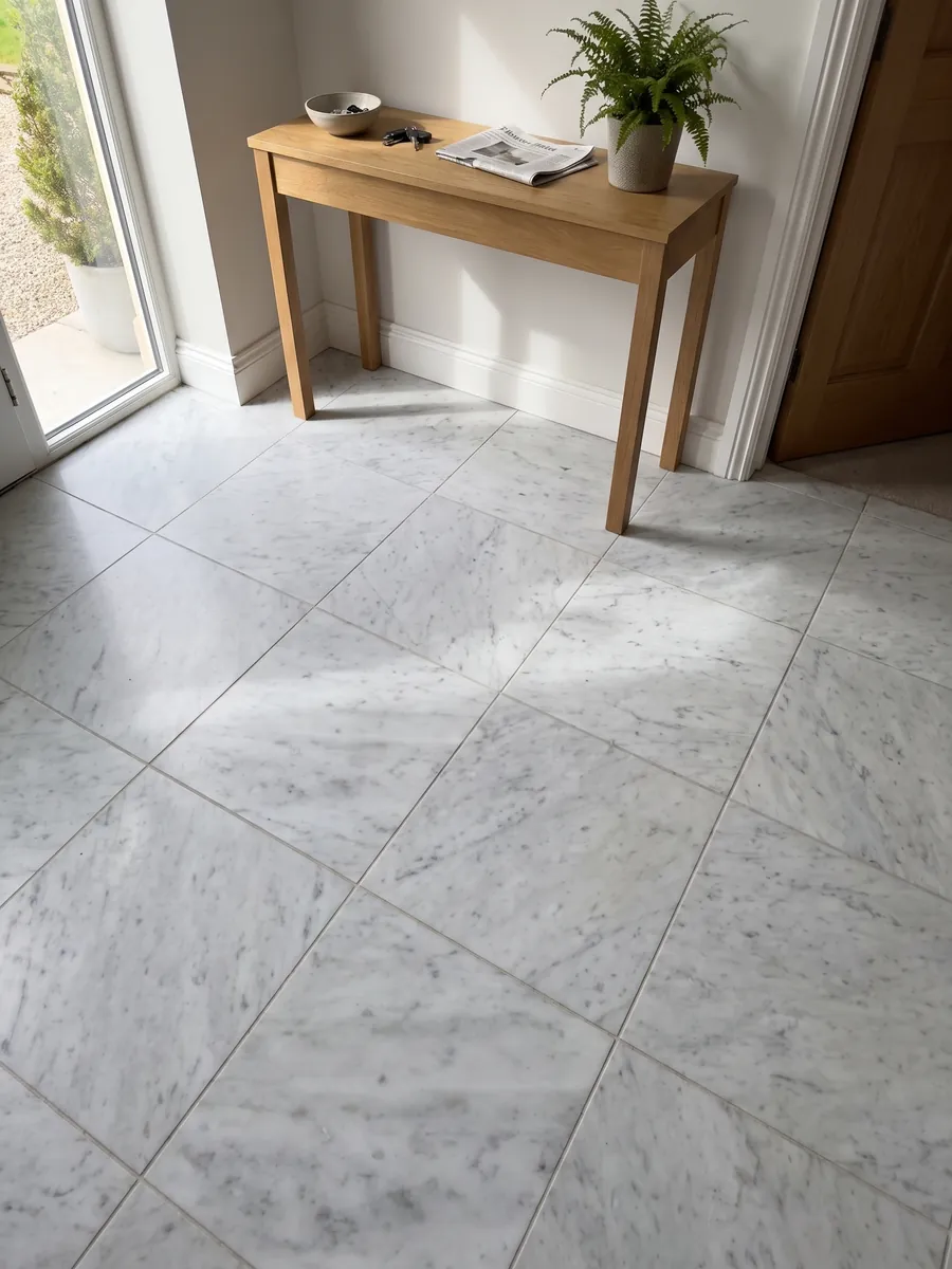 Entryway floor in large slabs of white Carrara CD marble with natural light: grayish white with diffuse gray patches on the diagonal