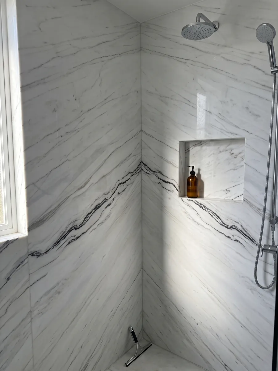 Shower clad in full slabs of Bianco Covelano Macchia Vecchia marble with a recessed niche: white with a wavy black vein crossing the slab almost horizontally