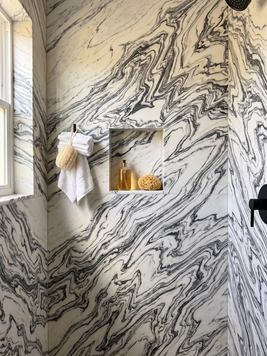 Shower clad in full slabs of white Fantastico Arni marble with a recessed niche: black veins folded in a zigzag forming continuous waves over a white background