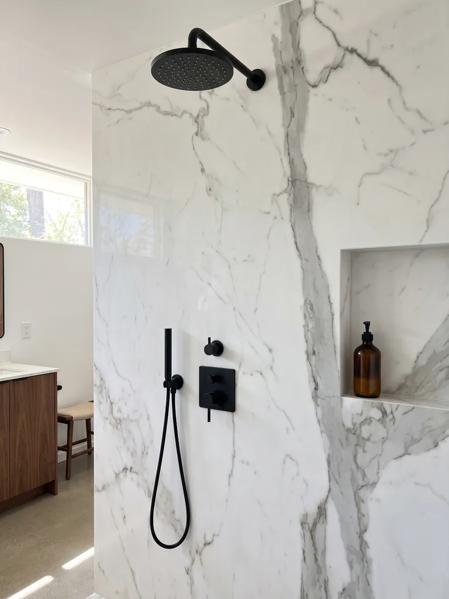 Shower clad in full slabs of white Geneva marble with a recessed niche: very clean white crossed by a vertical gray vein and a few fine branches