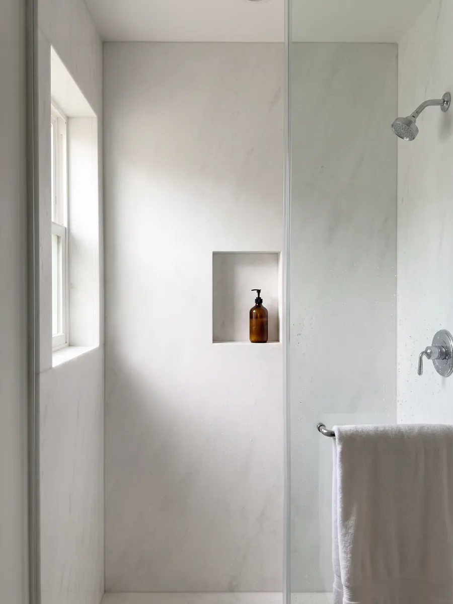 Shower clad in full slabs of Bianco Ghiaccio marble with a recessed niche: pure white with almost no visible pattern