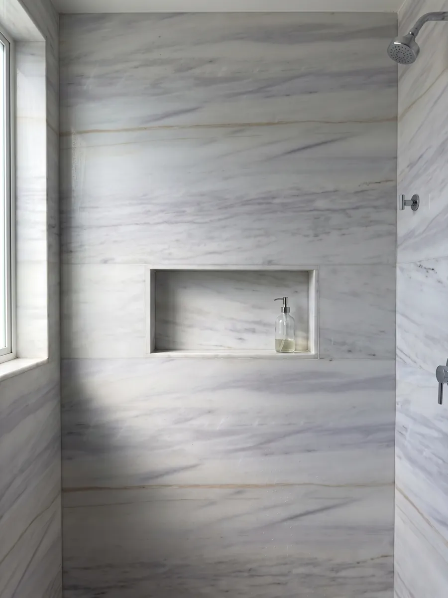 Shower clad in full slabs of Bianco Lasa Covelano Gold marble with a recessed niche: grayish white with soft horizontal lavender veins and one fine gold line