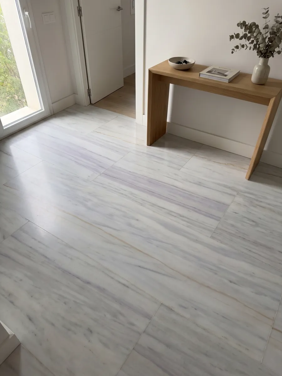 Entryway floor in large slabs of Bianco Lasa Covelano Gold marble with natural light: grayish white with soft horizontal lavender veins and one fine gold line