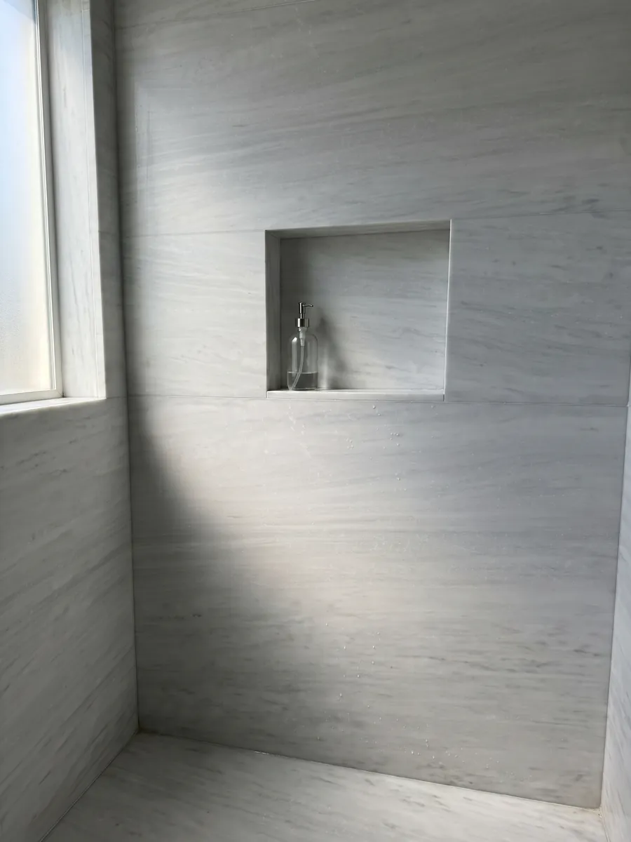 Shower clad in full slabs of Bianco Laser marble with a recessed niche: nearly plain grayish white with very soft horizontal lines