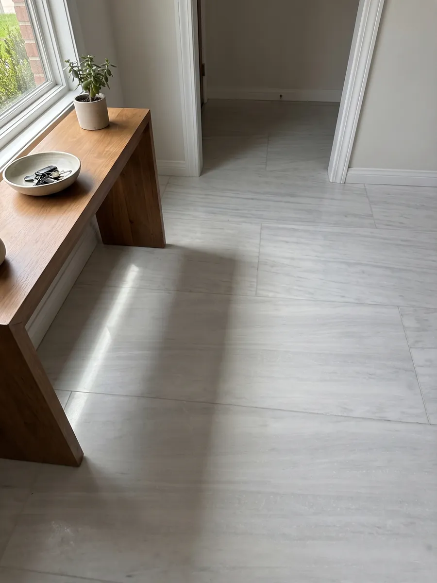 Entryway floor in large slabs of Bianco Laser marble with natural light: nearly plain grayish white with very soft horizontal lines