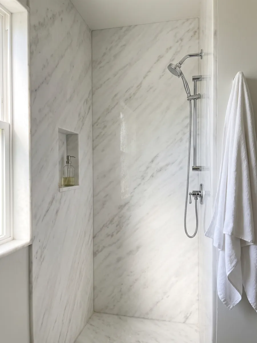 Shower clad in full white Namibia Cream marble slabs with a recessed niche: almost plain white with very faint gray clouds