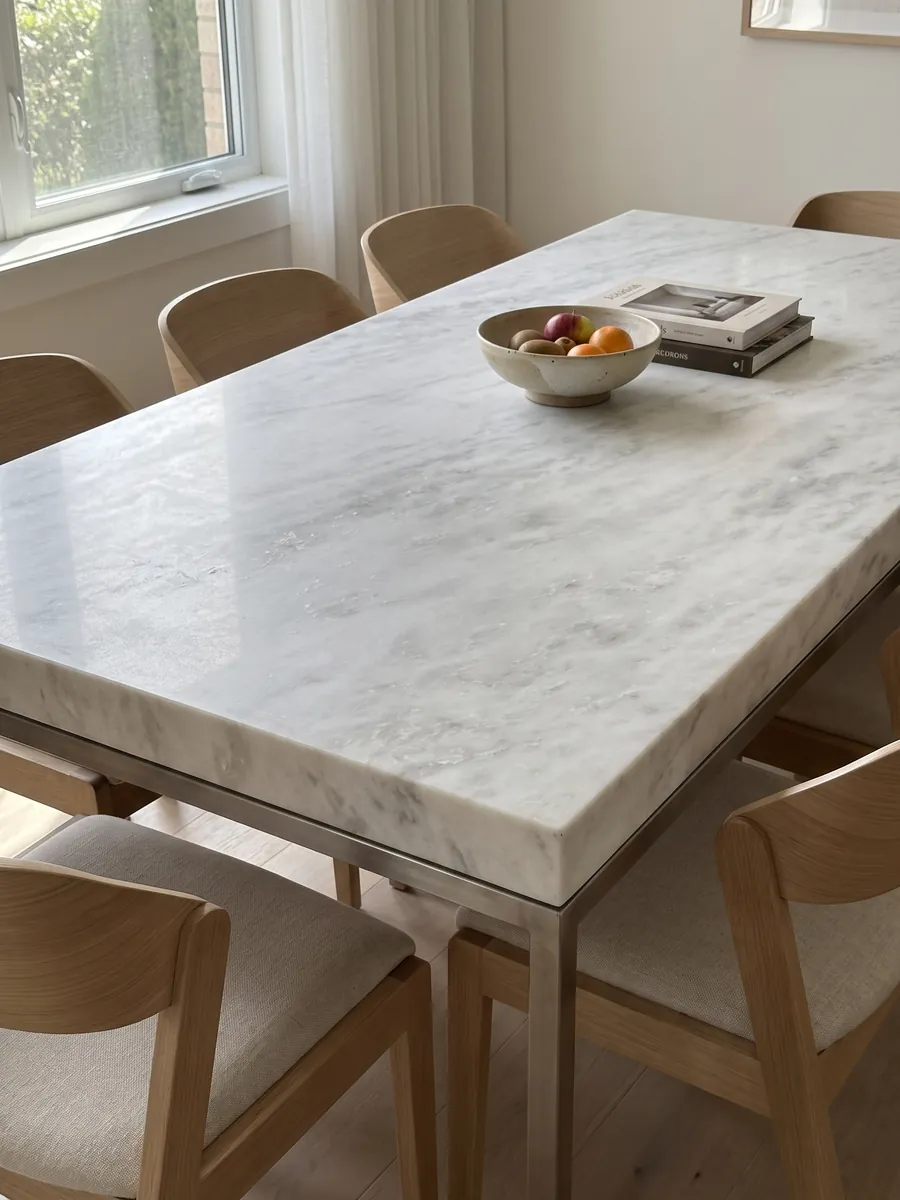 Dining table with a white Namibia Cream marble top on a steel base: almost plain white with very faint gray clouds