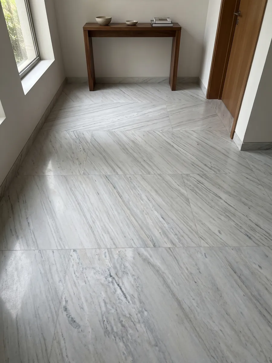 Entryway floor in large slabs of white Palissandro marble with natural light: grayish white with fine parallel gray strokes on the diagonal