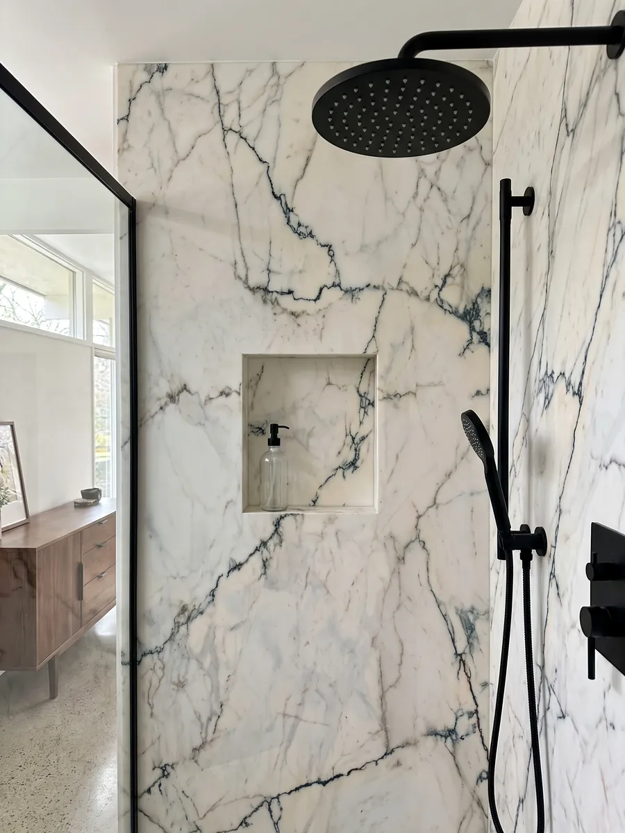 Shower clad in full slabs of white Paonazzo marble with a recessed niche: warm white with fine dark teal veins that look like cracks