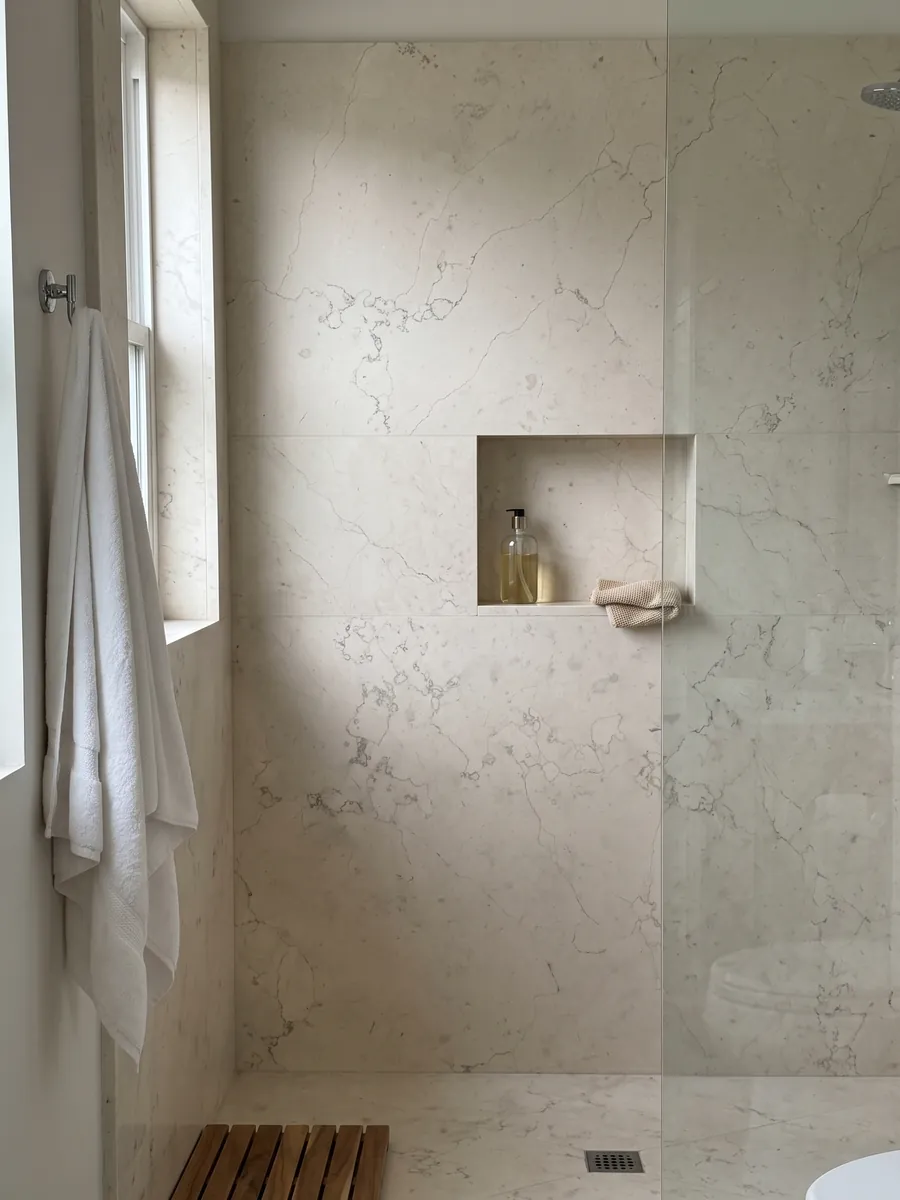 Shower clad in full Bianco Perlino marble slabs with a recessed niche: smooth ivory with scattered very fine thread-like gray veins