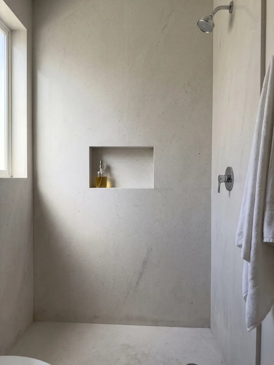 Shower clad in full Bianco Siberia marble slabs with a recessed niche: plain grayish white with small scattered dark dots
